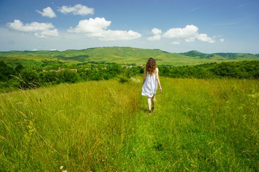 A wide shot of a young woman in a dress walking in a grassy field on a cool and cloudy day