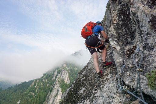 A wide shot of a young man climbing up a cliff on a cold and foggy day