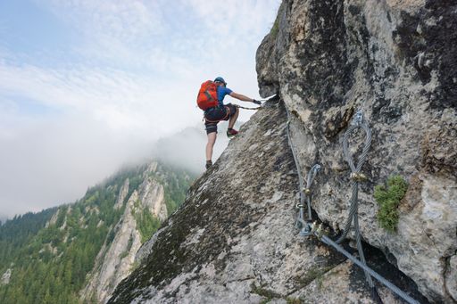A stunning shot of a young man climbing up a cliff on a cold and foggy day