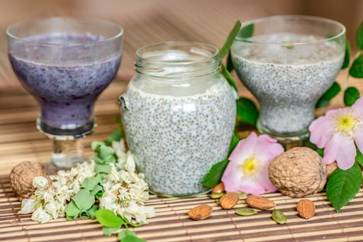 A top view of chia seed pudding with dog-rose flowers, almond milk, and nuts on glass containers