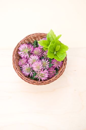 A vertical shot of red clovers in a basket on a wooden surface with space for text
