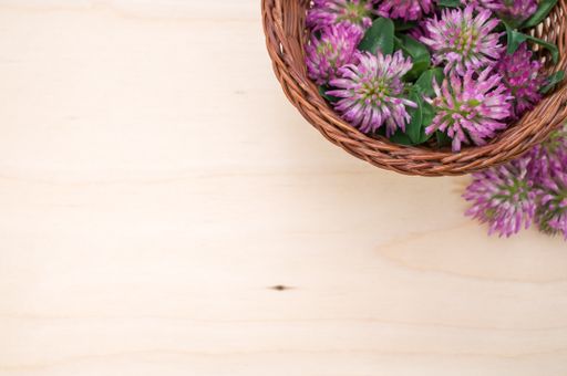 A top view of red clovers in a basket on a wooden surface with space for text