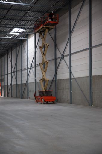 A scissor lift in an empty warehouse. On the platform near the roof is an engineer fixing the roof.