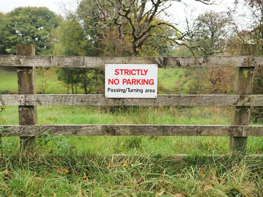 Close-up of a wooden fence with two signs that read "Strictly No Parking in This Field" prominently displayed