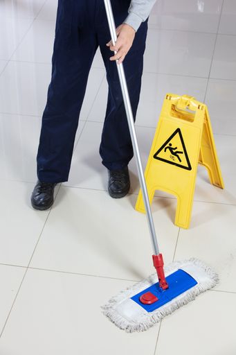 A person cleaning the floor with a flat mop near a yellow caution wet floor sign