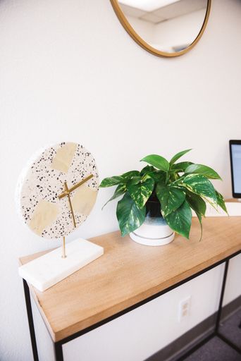 A vertical shot of a clock design with house plant in a table and a mirror on a white wall
