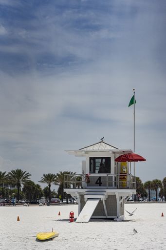 A vertical shot of a small hut on a white sandy beach under a bright cloudy sky