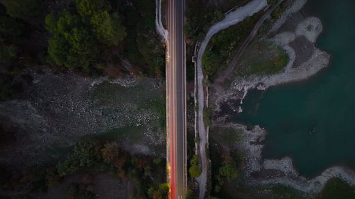 An aerial shot of an expansive bridge crossing a tranquil river, surrounded by lush green foliage.