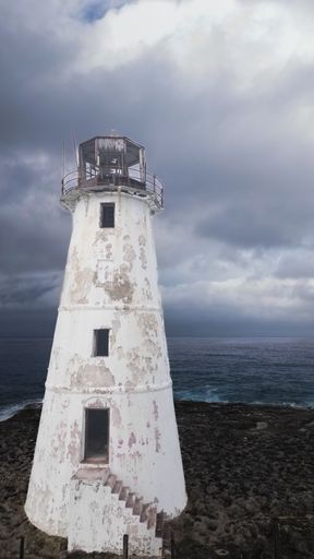 A majestic white lighthouse perched atop a rocky cliff overlooking the vast expanse of the ocean