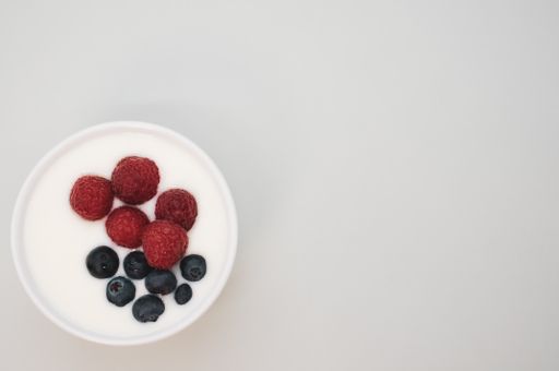 A closeup shot of a ceramic bowl of white yogurt with blueberries and raspberries