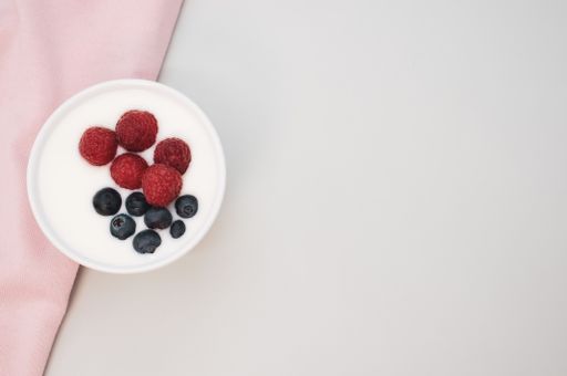 A closeup shot of a ceramic bowl of white yogurt with blueberries and raspberries