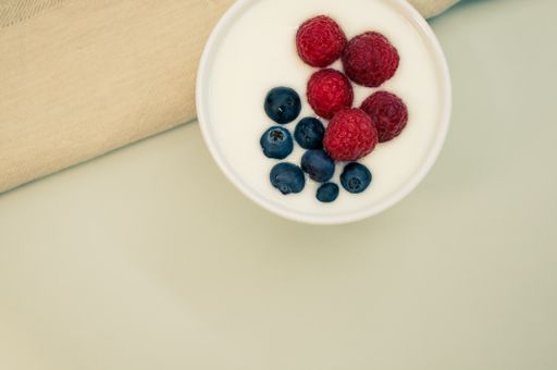 A closeup shot of a ceramic bowl of white yogurt with blueberries and raspberries