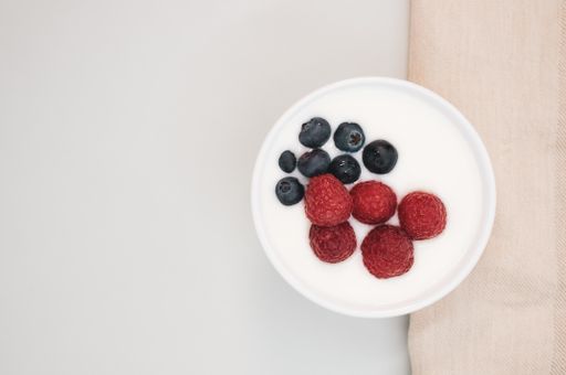 A closeup shot of a ceramic bowl of white yogurt with blueberries and raspberries