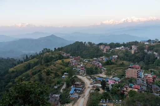 A small town nestled at the foot of a mountain range is illuminated by the warm glow of the setting sun in the background