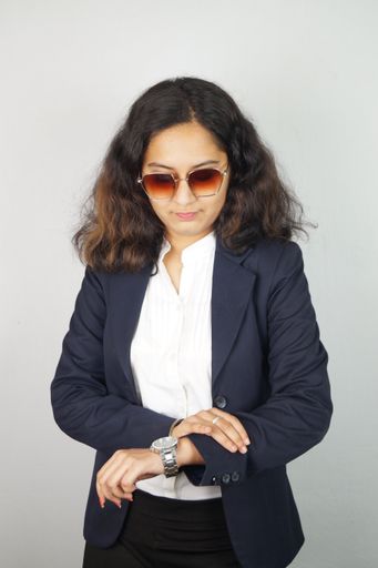 A confident Indian businesswoman with sunglasses looking at her watch standing against a white wall