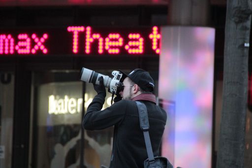 A man with a digital camera is capturing a stunning shot of a cityscape with a computer monitor visible in the foreground