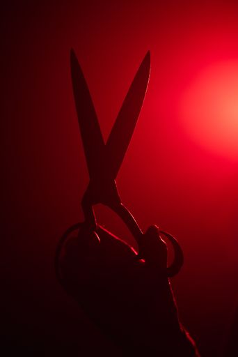 A vertical shot of a hand holding a large pair of scissors with a bright red run shining behind