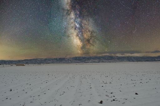 The Milky way over a field covered with snow with mountains in background
