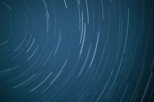 A horizontal background of star trails on a bright blue sky