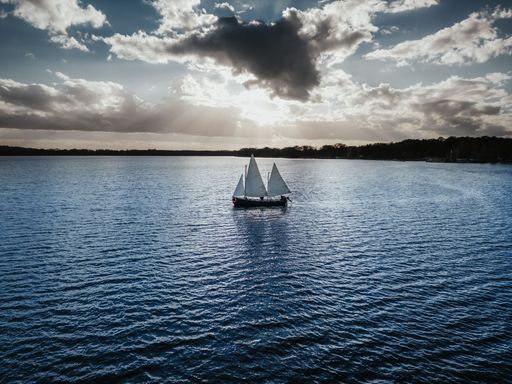 A wooden boat is moored at nightfall, illuminated by the setting sun, while the tranquil water reflects its warm rays