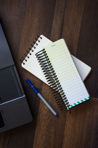 A top view of a wooden desk with a notebook, and a pen next to a laptop computer.