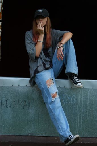 A young woman in a stylish outfit taking a break and enjoying a cigarette seated on a stone wall