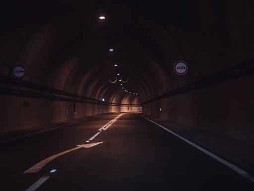 A dark single lane underground tunnel road with little light