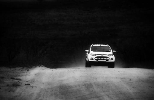 A white sedan car driving along a dirt country road, surrounded by a picturesque landscape of rolling hills and tall grass