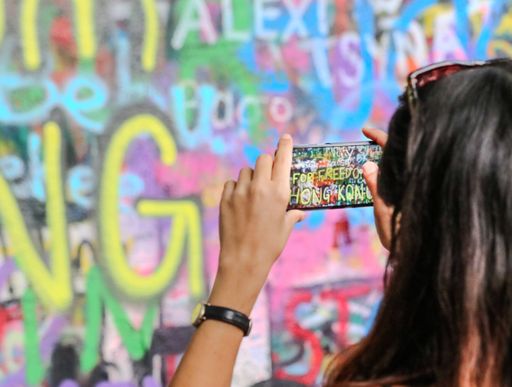 A young female photographer taking a photograph of a colorful graffiti mural painted on the side of an urban wall