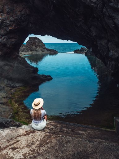 A vertical shot of a blonde woman wearing a hat, enjoying the view of the calm water