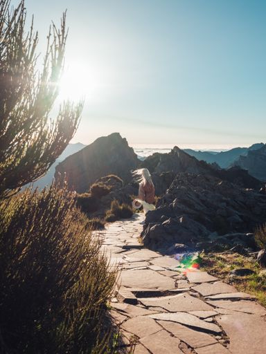 A vertical shot of a female from back holding a hat in her hand walking on the stone road amid rocks