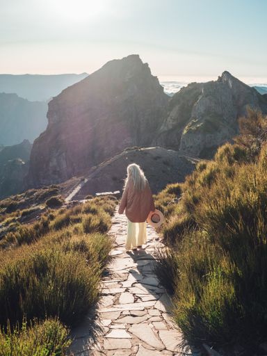 A vertical shot of a blonde woman hiking on a trail in the mountains, enjoying the beautiful view