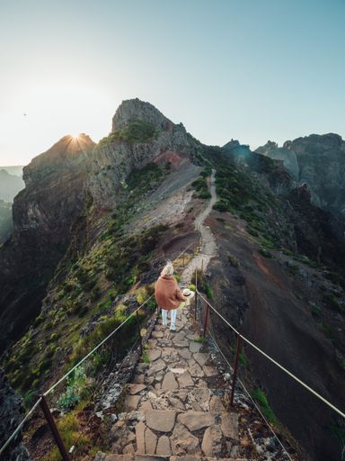 A vertical shot of a blonde woman hiking on a trail in the mountains, enjoying the beautiful view