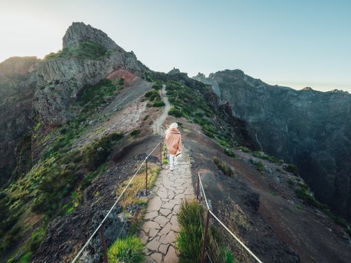 A woman walking on a narrow stone footpath on the hill with mountains in the background at sunset