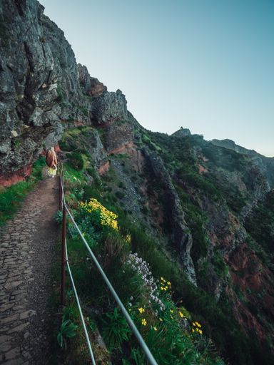 A back view of a woman walking on a stone narrow footpath on a rocky mountainside at sunset