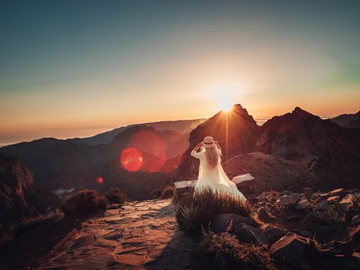 A female from a back in a white dress and hat in a rocky area at sunset