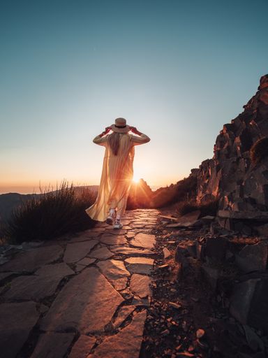 A vertical shot of a blonde woman on a trail in the mountains, enjoying the beautiful view during sunset