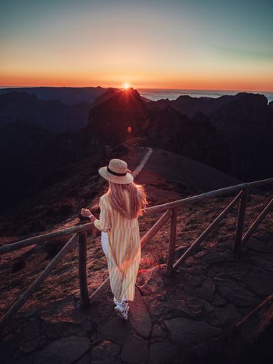 A vertical shot of a blonde woman on a trail in the mountains, enjoying the beautiful view during sunset