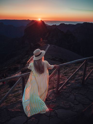 A vertical shot of a blonde woman on a trail in the mountains, enjoying the beautiful view during sunset