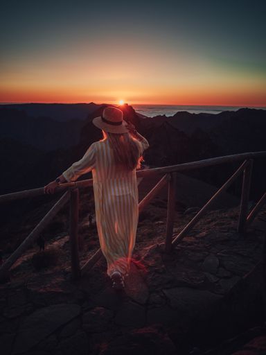 A vertical shot of a blonde Caucasian girl on a path in the mountains, enjoying the view during sunset