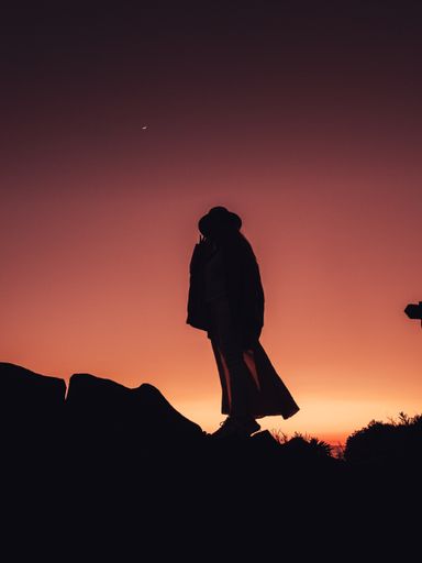 A vertical silhouette shot of a woman out in nature during sunset