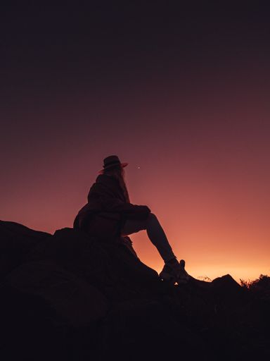 A vertical silhouette shot of a girl on a path in the mountains, enjoying the view during sunset