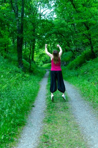 A vertical shot of a happy female jumping on a pathway in a green forest