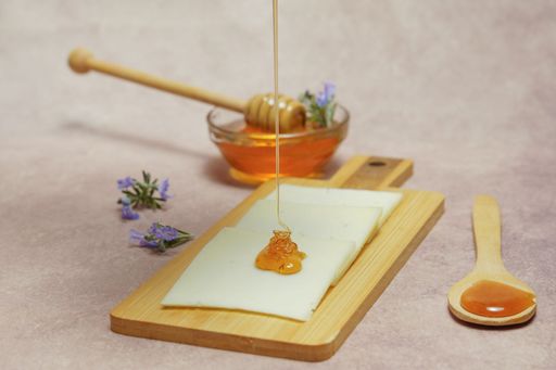 drizzle of honey dripping on cheese slices with fresh rosemary branches in bloom and a glass bowl with rosemary honey.