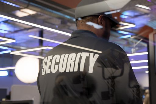A security guard standing inside a commercial building nearby the window reflecting light