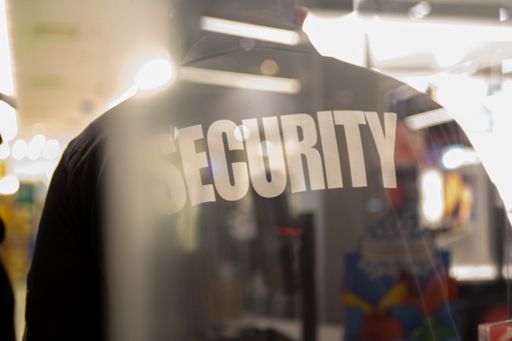 A security guard standing inside a commercial building nearby the window reflecting light.