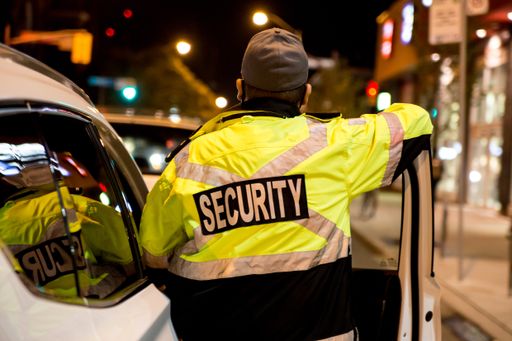A rear view of a security guard standing next to a security car at night city.