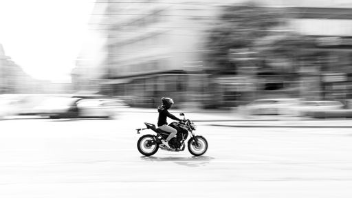 An adult male wearing a helmet and riding a motorcycle speeds through an intersection on a city street