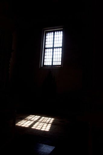 A vertical shot of a dark room with sunlight passing through the window and lighting up the floor