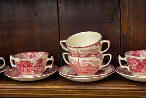 An array of delicate porcelain teacups and saucers displayed on a wooden shelf